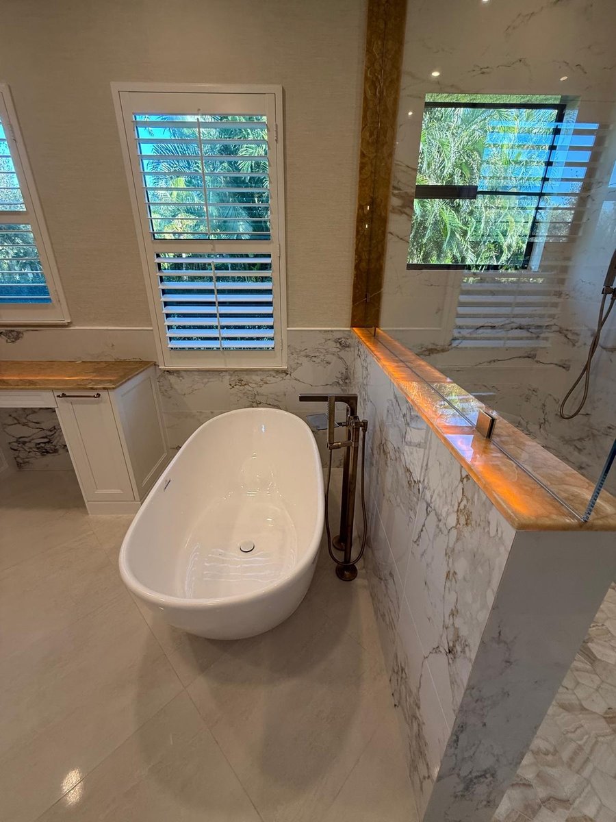full home remodel primary bathroom with freestanding tub glass shower and marble look walls in naples fl